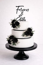 Load image into Gallery viewer, May include: A three-tiered white wedding cake with black rose floral arrangements and a black cake stand. The cake is decorated with black ribbon and a topper that reads "Forever & Ever Smith."