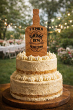 Load image into Gallery viewer, May include: A two-tiered cake with white icing and decorative swirls, topped with a wooden sign shaped like a bottle. The sign reads "Stephen Vintage 1974 Perfection". The cake is on a wooden surface.