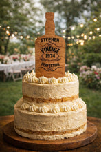 Load image into Gallery viewer, May include: A two-tiered cake with white icing and decorative swirls, topped with a wooden sign shaped like a bottle. The sign reads "Stephen Vintage 1974 Perfection". The cake is on a wooden surface.