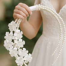 Load image into Gallery viewer, May include: A white bridal bouquet with large, white flower details and strands of faux pearls. The bouquet is held by a white satin ribbon. The flowers are clustered, creating a cascading effect.
