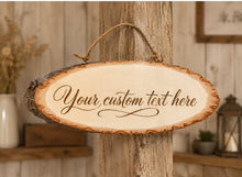 Load image into Gallery viewer, Personalised rustic wood slice hanging sign with “Your custom text here” engraved in script font. Natural bark-edge wooden plaque with rope hanger, displayed against a neutral rustic venue background.
